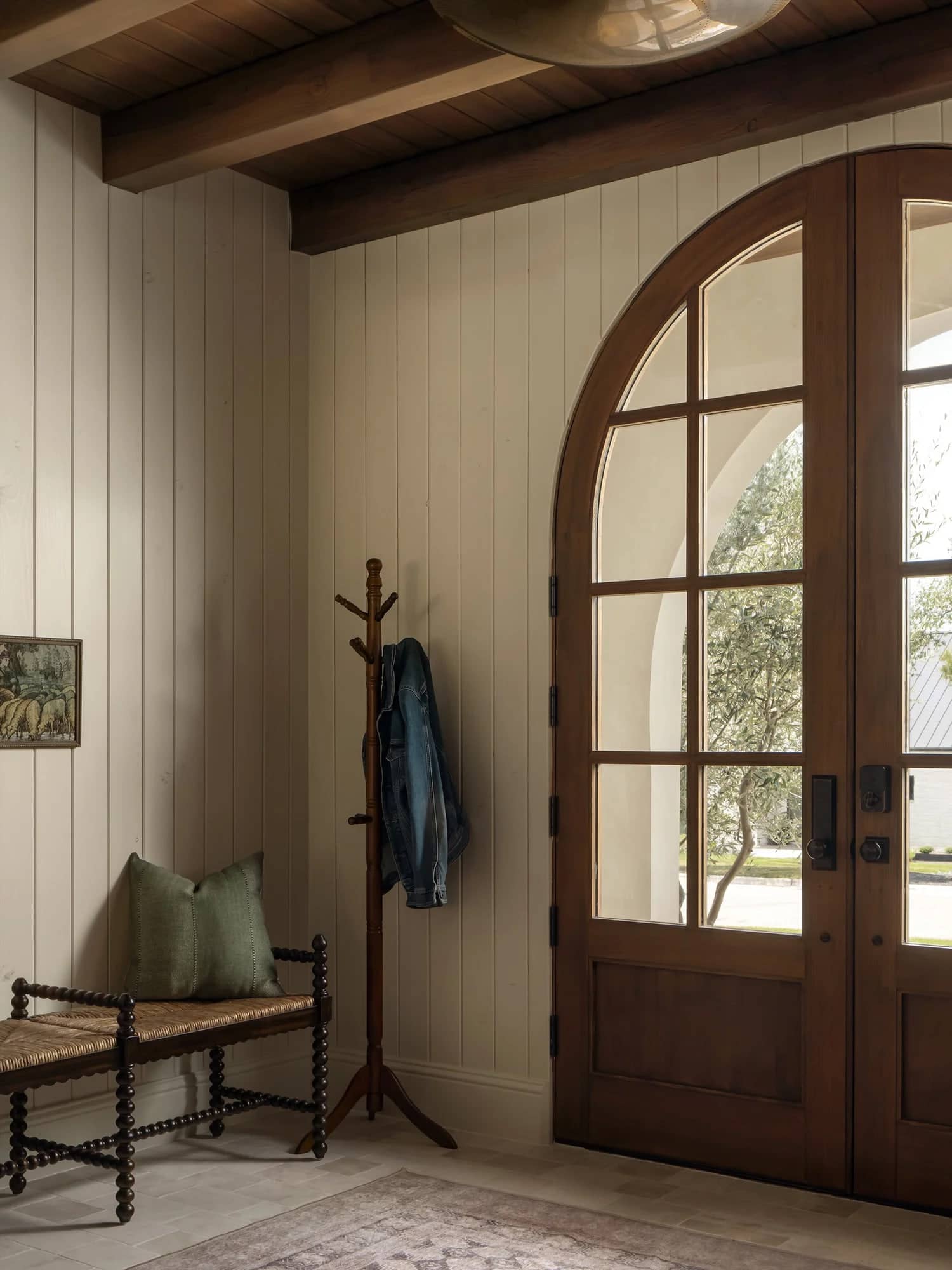 An entry hall with a console table under a tall mirror, light falling across a stone floor.