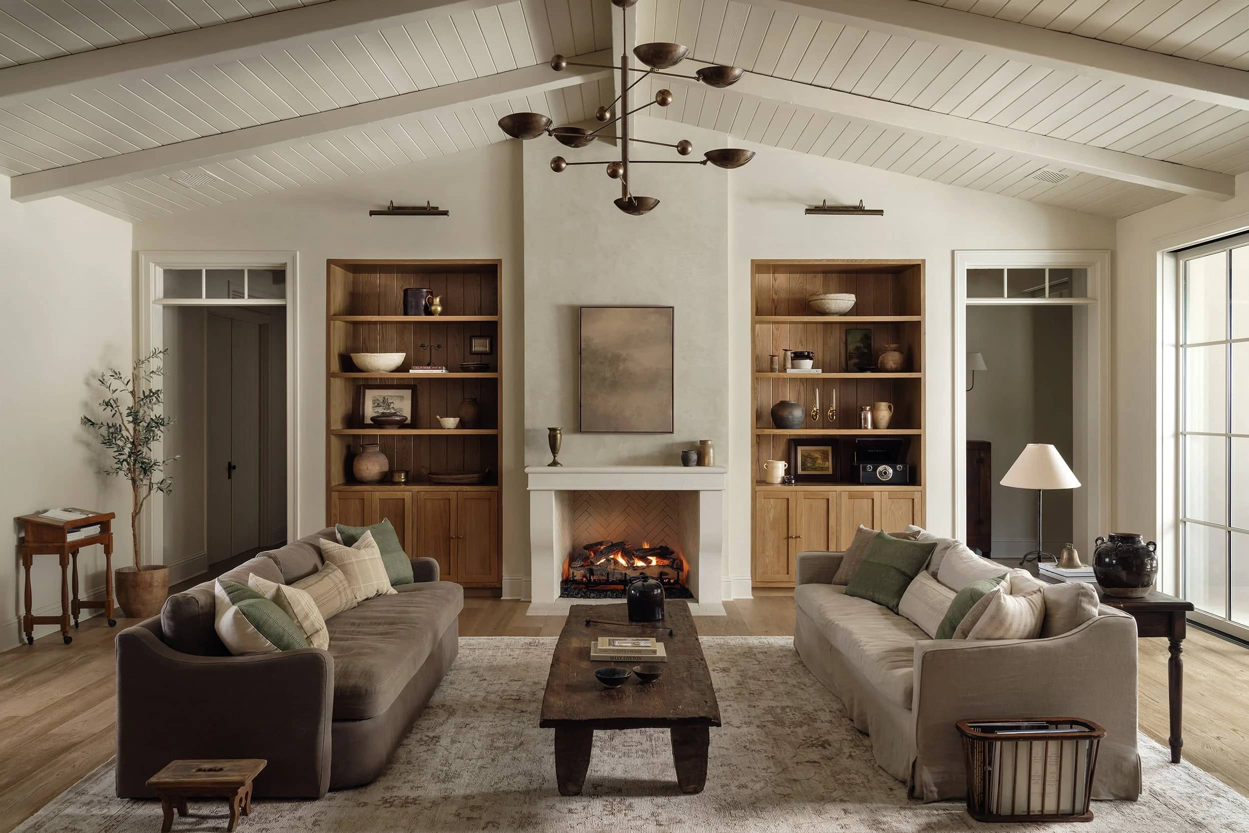 A living room with a limestone fireplace set between white oak built-ins, under a vaulted beadboard ceiling.